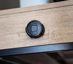 Round black biometric safe keypad attached to a light wood drawer, security device visible
