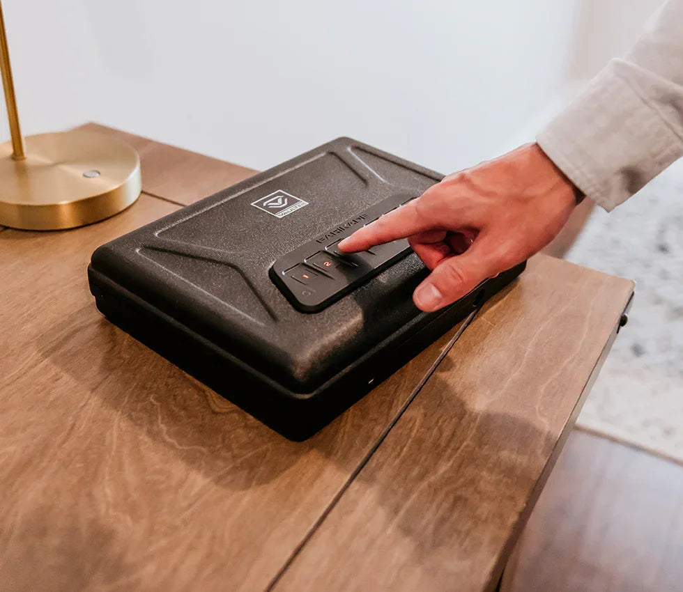 Person using keypad on black biometric safe on wooden table in home setting