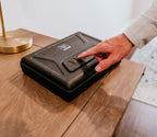 Person using keypad on black biometric safe on wooden table in home setting