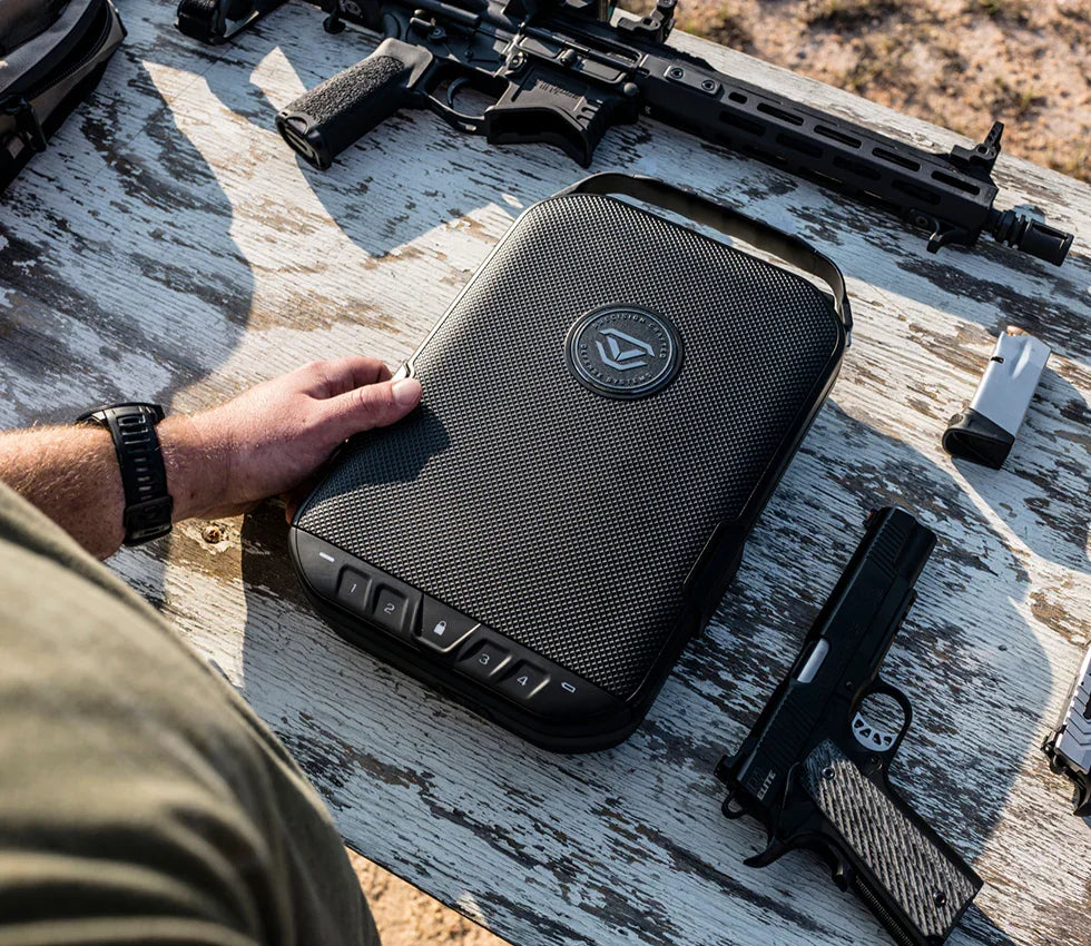 Durable portable gun safe with carry handle on outdoor wooden table near firearms and magazine.