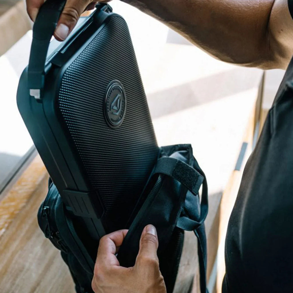 Person placing a rugged portable safe into a black travel bag, perfect for secure transport.