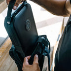Person placing a rugged portable safe into a black travel bag, perfect for secure transport.