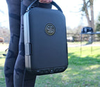 Person carrying a portable biometric safe with keypad outdoors on a grassy area