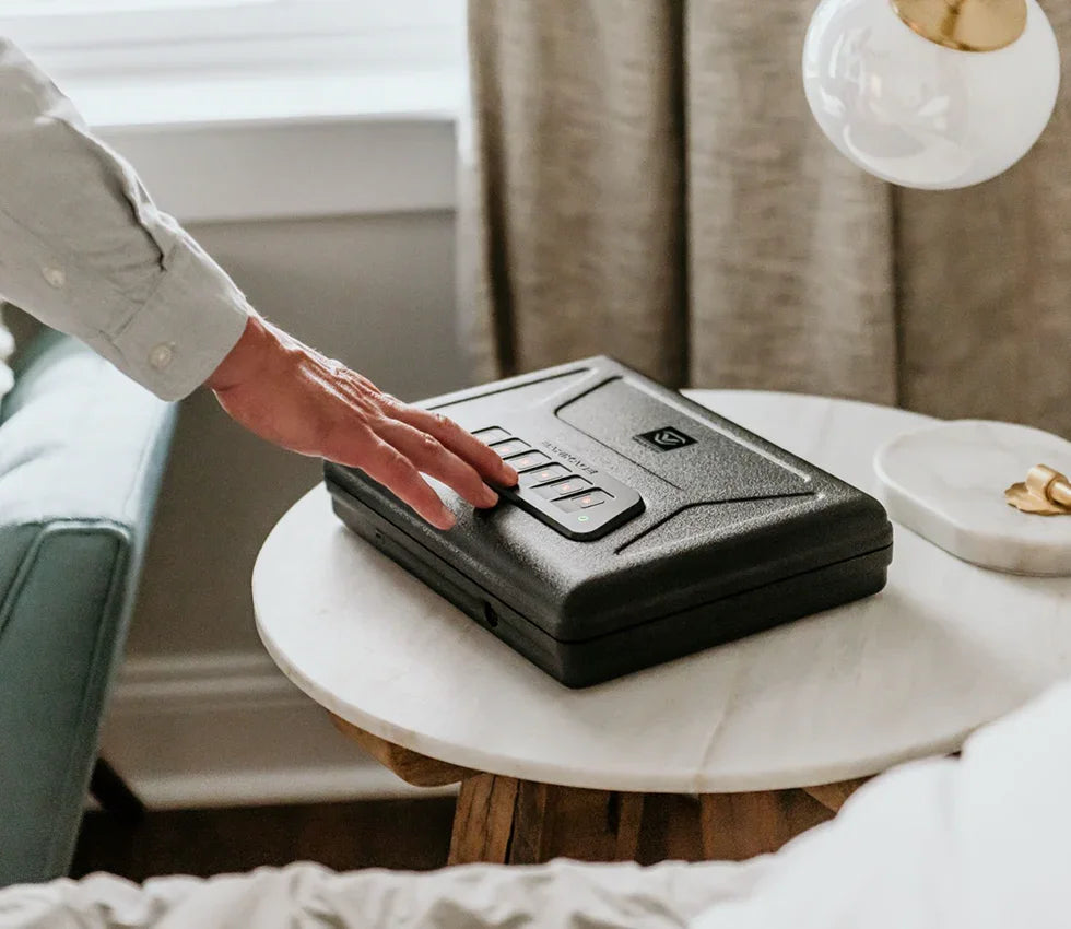 Person securing a biometric safe with keypad on a bedroom nightstand