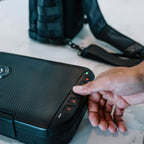 Person unlocking compact travel safe with keypad, black tactical bag in background