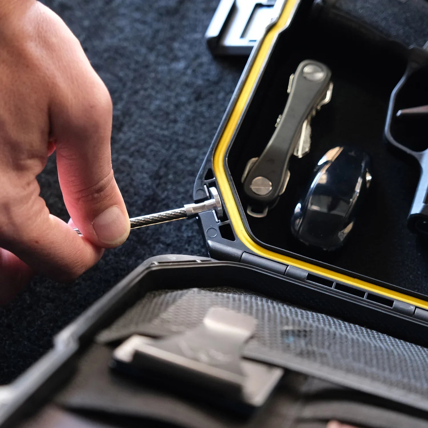 Hand securing portable waterproof safe with yellow seal, holding keys and car fob inside