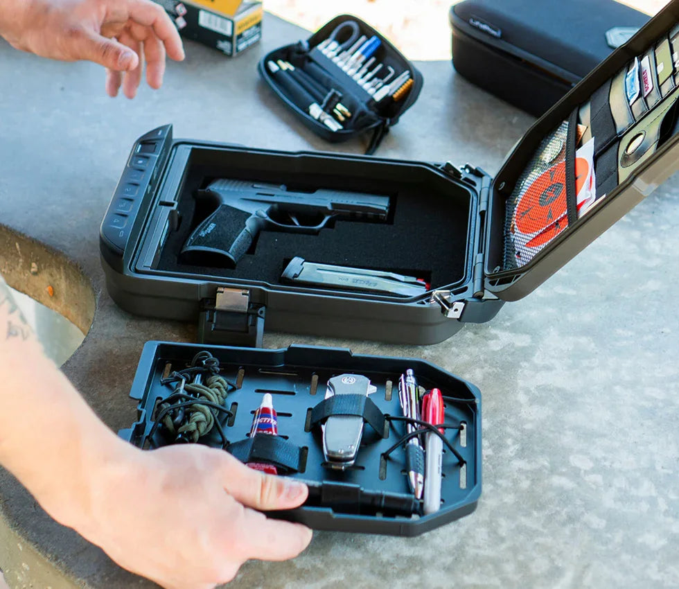 Portable biometric safe open on a table holding a handgun, magazine, and everyday essentials.