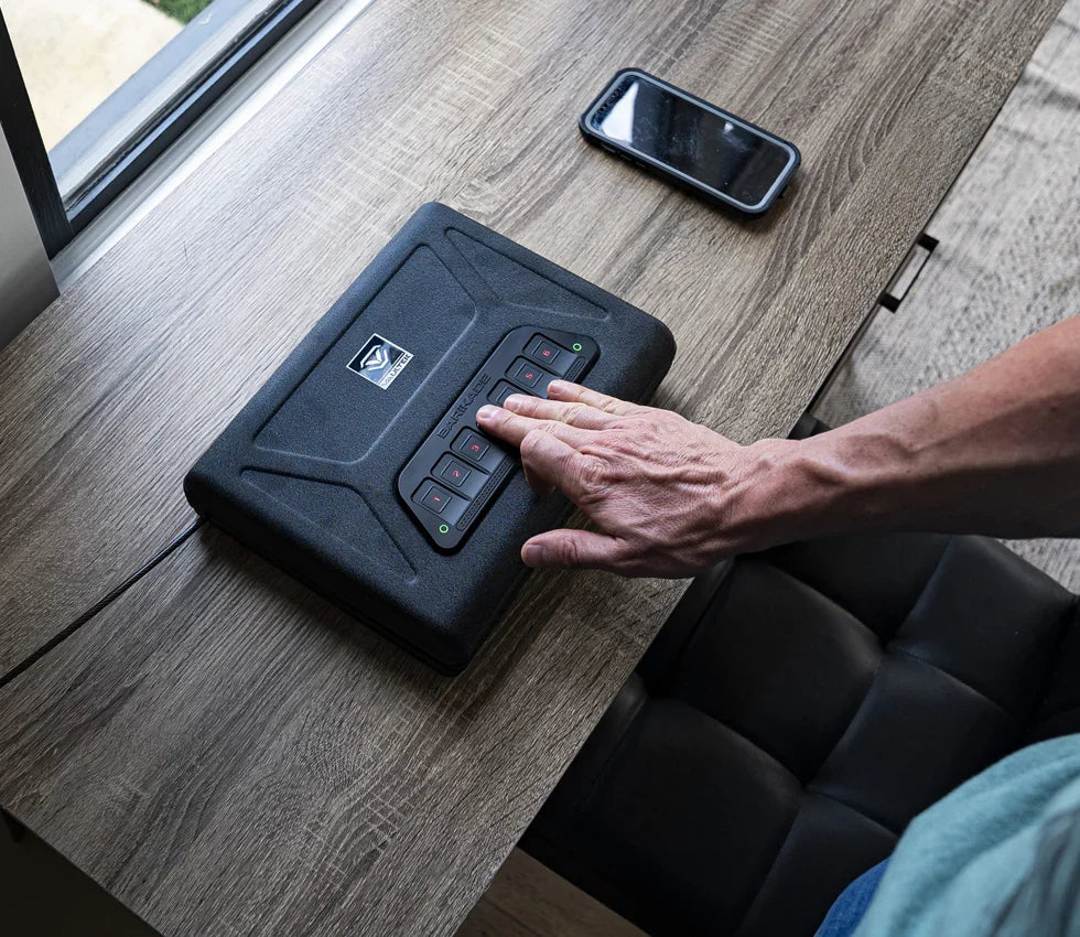 Person using fingerprint keypad on a biometric safe box on wooden desk near smartphone