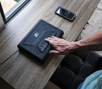 Person using fingerprint keypad on a biometric safe box on wooden desk near smartphone