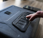 Hand entering code on textured keypad of electronic safe on wooden surface