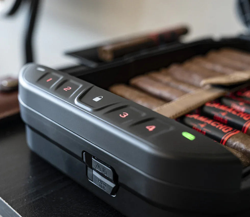 Close-up of a black biometric safe storing cigars on a table, with keypad and indicator lights.