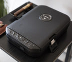 Textured biometric safe with keypad and lock, placed on a black table indoors