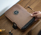 Hand opening a textured brown biometric safe with keypad on a wooden table, next to keys and cigar.