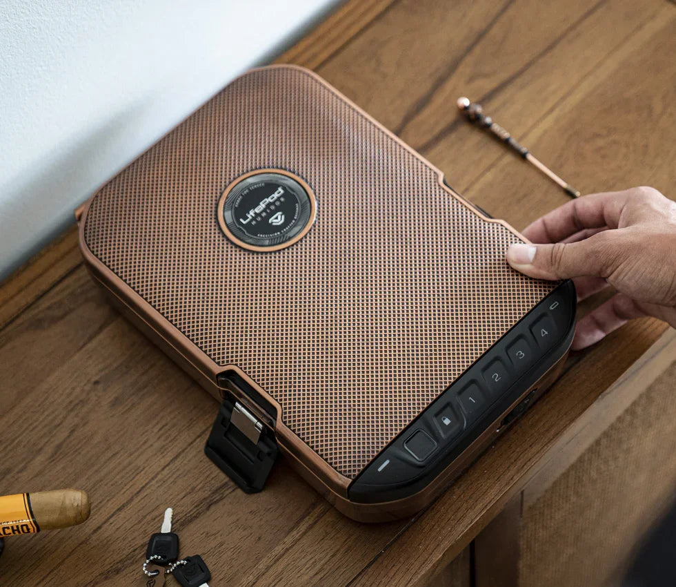 Hand opening a textured brown biometric safe with keypad on a wooden table, next to keys and cigar.