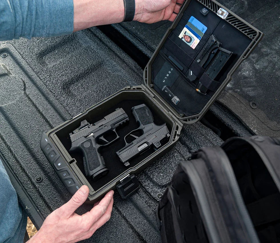 Portable lockbox safe open in a car trunk holding two handguns, magazines, and ID cards.