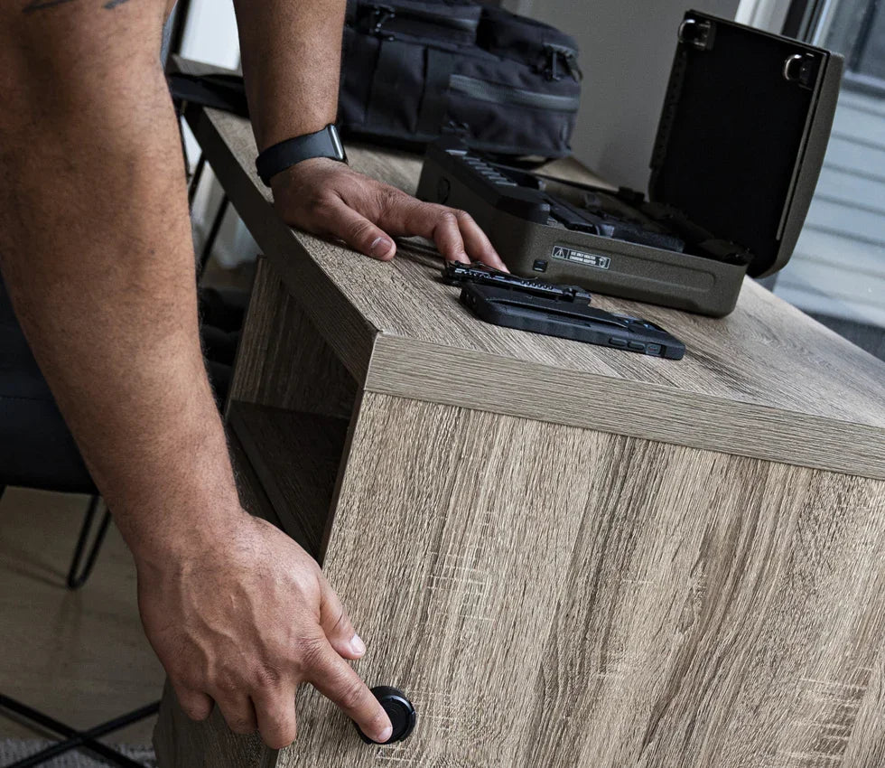 Person activating hidden drawer in wood desk near portable biometric safe and keys
