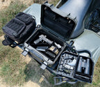 Open portable safe on ATV with handgun, magazines, binoculars, and tactical gear outdoors