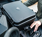 Rugged portable safe with textured lid and logo, secured outdoors by a person’s hand