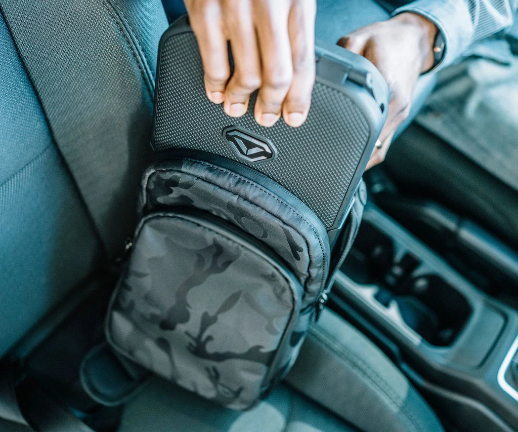Person placing compact biometric safe into camouflage travel bag on car seat