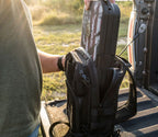Person placing portable biometric safe into rugged black tactical backpack outdoors