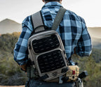 Man wearing tactical sling backpack outdoors, durable bag for hiking or travel in wilderness