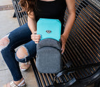 Woman placing a blue portable safe into a gray travel backpack on a bench